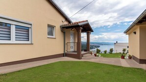 Ein Haus mit einer kleinen Veranda, einem Rasen und Blick auf eine Brücke und Wasser.