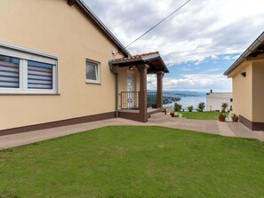 A house with a small porch, a grassy yard, and a view of a bridge and water. - Jadranka by Interhome (Opatija/Pobri)