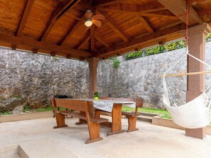 A covered outdoor area with a wooden bench, a hanging chair, and a stone wall.