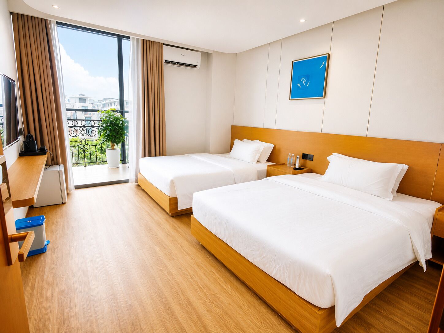 A hotel room with two beds, a desk, a TV, and a balcony with a plant.