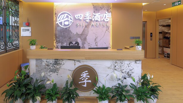 Un mostrador de recepción de hotel con encimera de mármol, plantas en macetas y un cartel con el nombre del hotel.