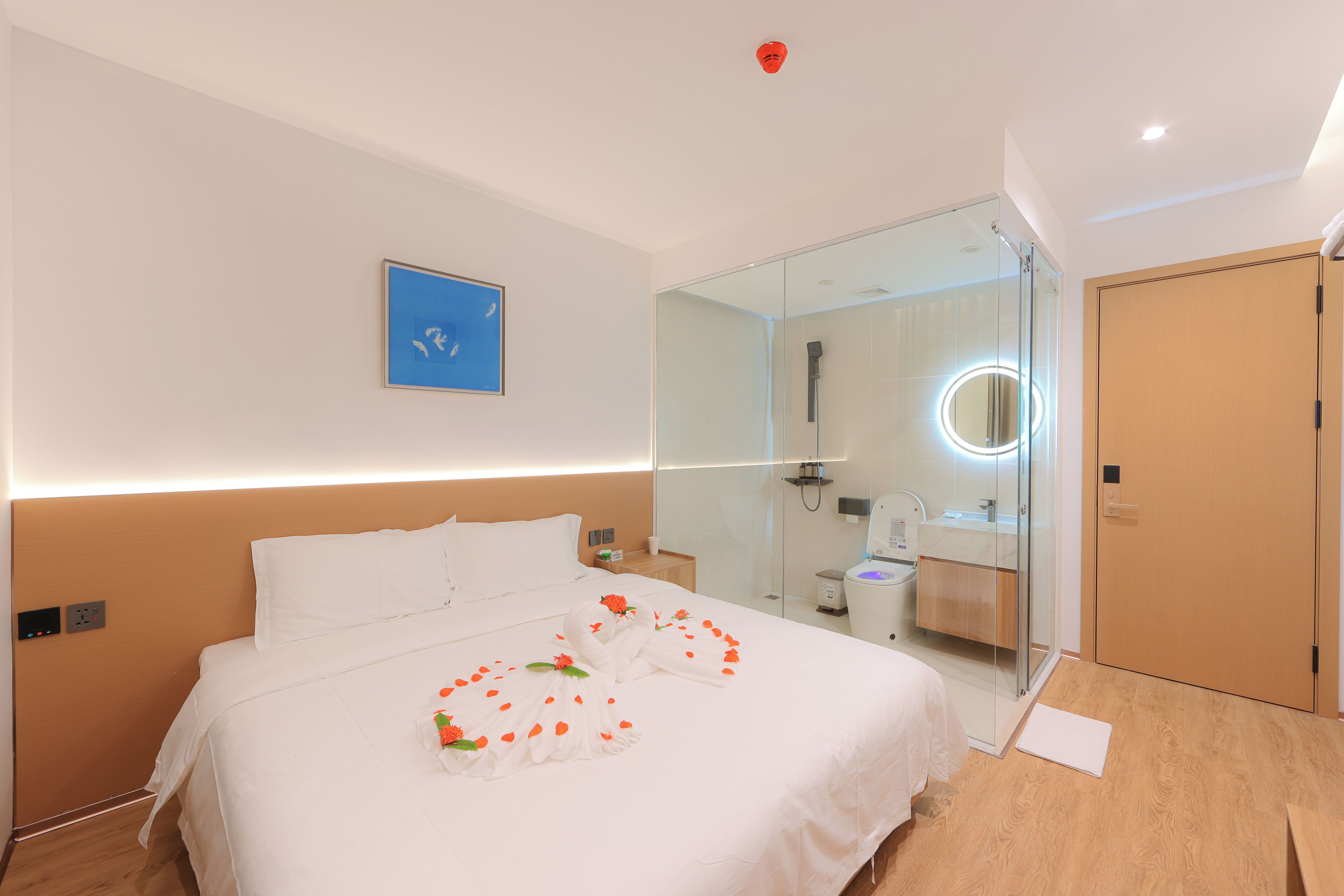 Een hotelkamer met een bed, een badkamer met een douchecabine van glas en een houten vloer.