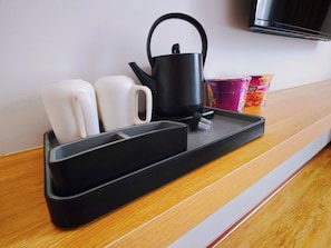 Una encimera de cocina con una tetera, dos tazas y una bandeja.