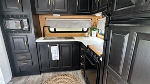A compact kitchen with dark cabinetry, a microwave, a stove, and a decorative rug on the floor.
