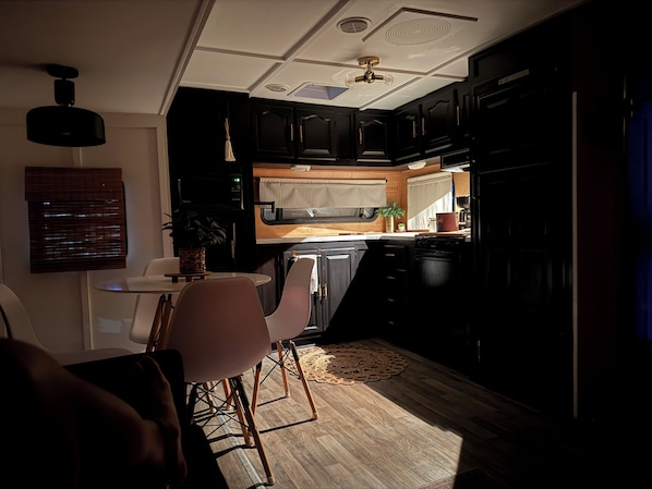 A compact kitchen with dark cabinetry, a dining area with a table and chairs, and a ceiling fan.