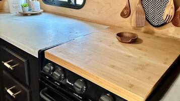 Una cocina compacta con encimera de madera, una estufa con varias hornillas, una ventana con cortinas a rayas y utensilios de madera colgando sobre la encimera.