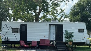 A white RV with a sliding door, two red chairs, a small table, and a potted plant.