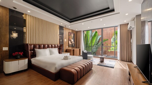 A modern bedroom with a large bed, wooden flooring, a TV, and a view of greenery. - Vidanang Luxury Villa - 6 Bedrooms - Pool - Sauna - Karaoke (Đà Nẵng)