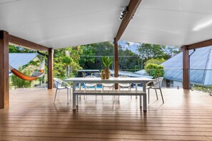 An outdoor patio with a wooden table and chairs, a hammock, and a view of a swimming pool and greenery. - The Perrins Lane Compound - Reset, Relax, Enjoy! (Arakoon)