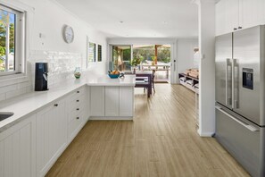 Una cocina moderna con armarios blancos, un refrigerador de acero inoxidable y un comedor con banco y mesa.