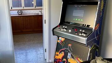Una habitación con una máquina de juegos de salón con temática espacial, una ventana con persianas y una puerta que da a otra habitación.