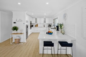 Una cocina moderna con armarios blancos, una isla central con taburetes de bar, un reloj en la pared y un cartel que dice 'hello'.