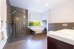 Een moderne badkamer met een vrijstaand bad, een douche met glazen wand en een groot raam met uitzicht op groen.