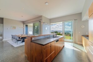 Een moderne keuken met een groot eiland, een eethoek met tafel en stoelen, en een uitzicht door grote schuifdeuren.