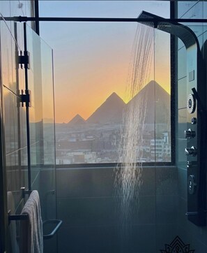 Une salle de bain moderne dotée d’une douche à parois de verre, d’un porte-serviettes et offrant une vue sur un paysage urbain avec des montagnes en arrière-plan.
