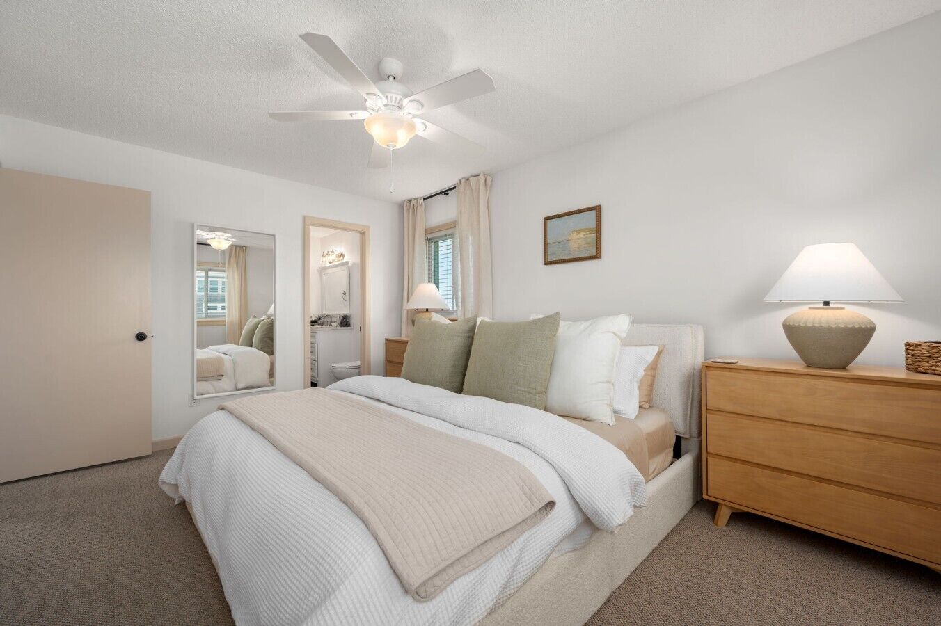 A bedroom with a bed, bedside table, lamp, and a ceiling fan.