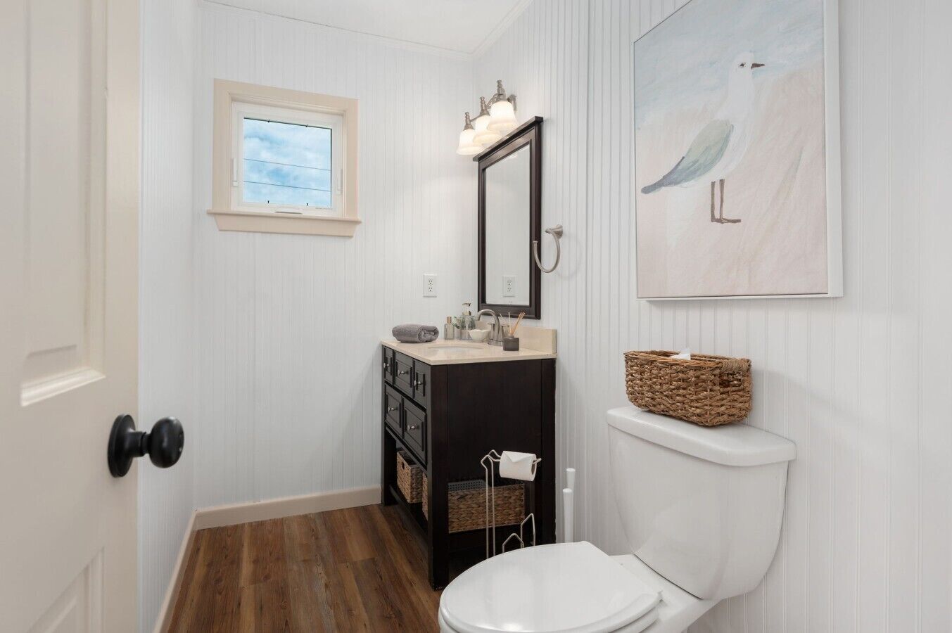 Un bagno con un water bianco, un lavabo con specchio, una finestra e un corpo illuminante a parete.