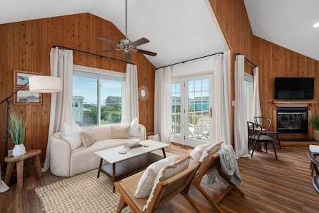 A spacious living room with a sofa, coffee table, and chairs, a fireplace, and large windows with curtains.
