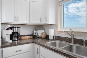 A kitchen with white cabinets, a coffee maker, a sink, and a window with a view of the sky.