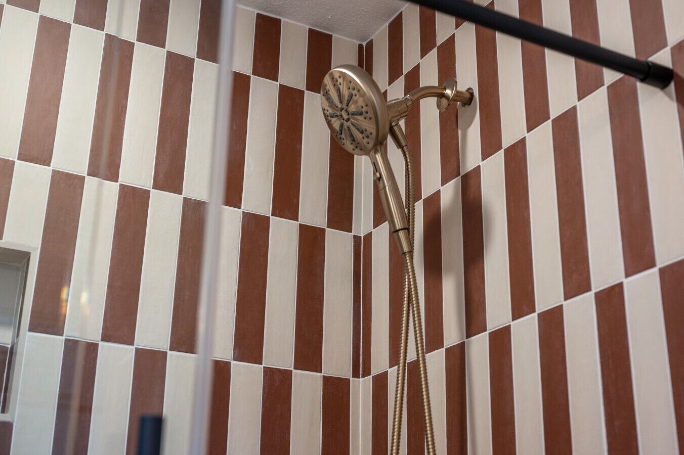 A bathroom with striped tile walls, a shower head, and a handheld shower attachment.