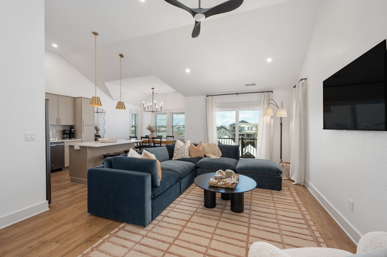 A modern living room with a sectional sofa, a coffee table, and a dining area with a kitchen in the background.