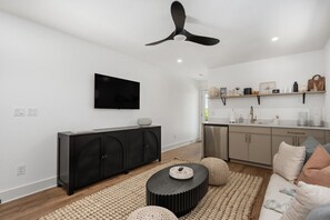 A modern living room with a flat-screen TV, a black entertainment unit, a round coffee table, and a ceiling fan. - New Beachside Home! Pool & Pet Friendly! (Kill Devil Hills)