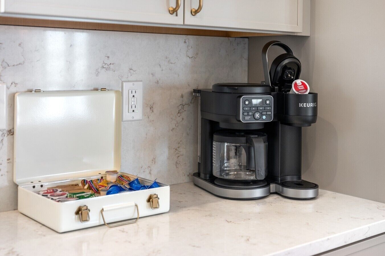 A coffee maker with a Keurig brand, a white travel case with compartments, and a marble countertop.