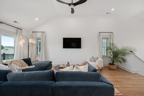 A modern living room with a sectional sofa, a flat-screen TV, and a potted plant. - New Beachside Home! Pool & Pet Friendly! (Kill Devil Hills)