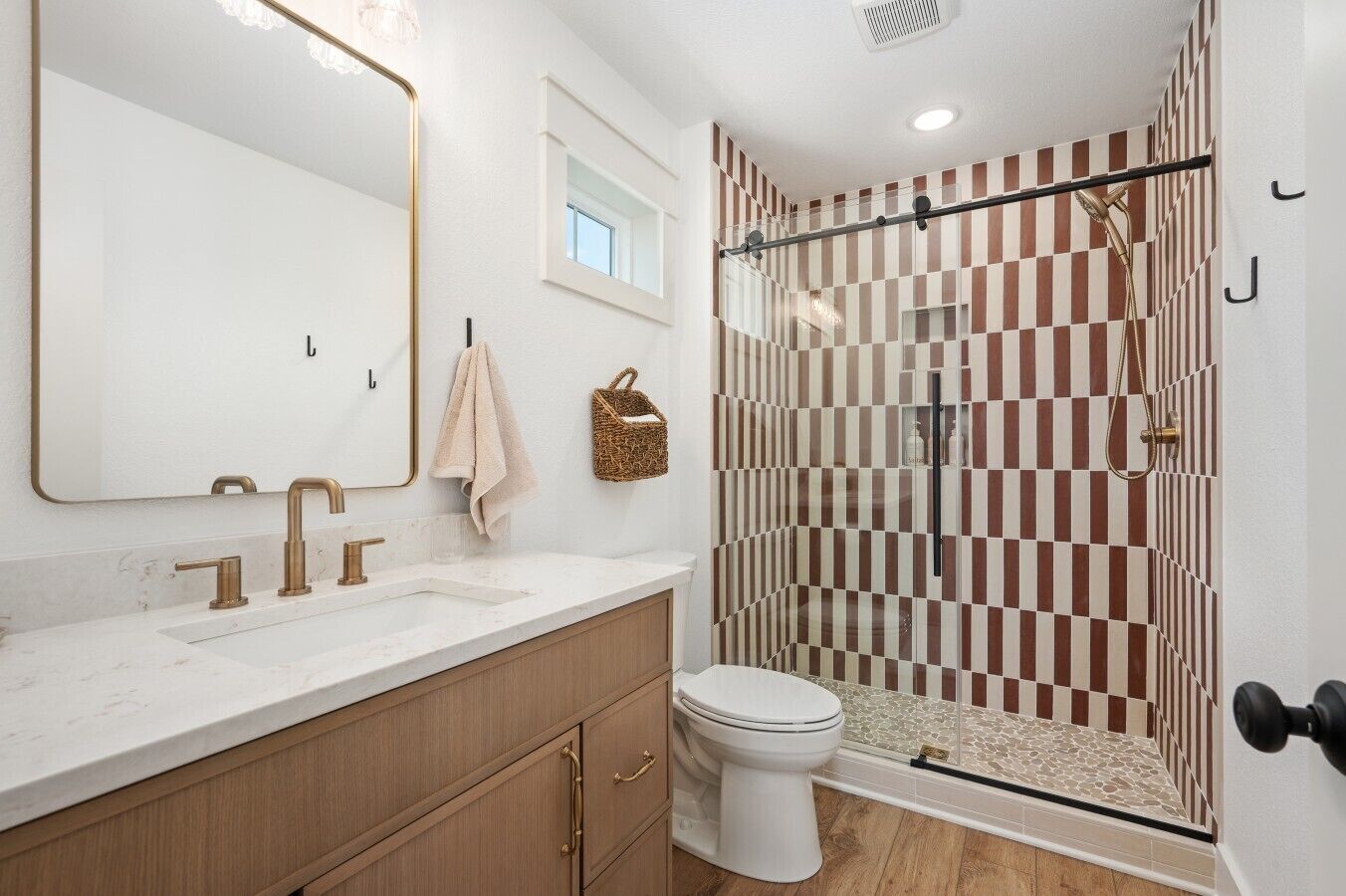 A bathroom with a large mirror, two sinks, a toilet, and a shower with a checkered tile pattern.