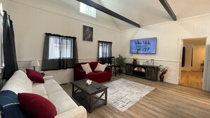 A spacious living room with a high ceiling, wooden beams, a large TV, and a cozy seating area. - Spacious Country Getaway (Guilford)