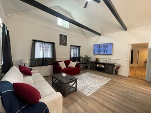 A spacious living room with a high ceiling, wooden beams, a large TV, and a cozy seating area.