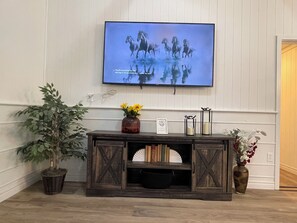 A television mounted on a wall displaying a horse race, a wooden console with decorative items, and a potted plant.
