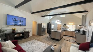 A spacious living area with a large TV, wooden flooring, a red sofa, a coffee table, and a kitchen in the background. - Spacious Country Getaway (Guilford)