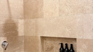 A shower with a handheld showerhead and a wall-mounted control valve. There is a shelf with three bottles labeled 'BODY WASH,' 'SHAMPOO,' and 'CONDITIONER.' - Luxe Apt. in Montebello Pool/Game Room/ Workspace (Mérida)