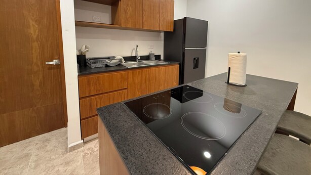 A modern kitchen with wooden cabinets, a black refrigerator, and a built-in stove. - Luxe Apt. in Montebello Pool/Game Room/ Workspace (Mérida)