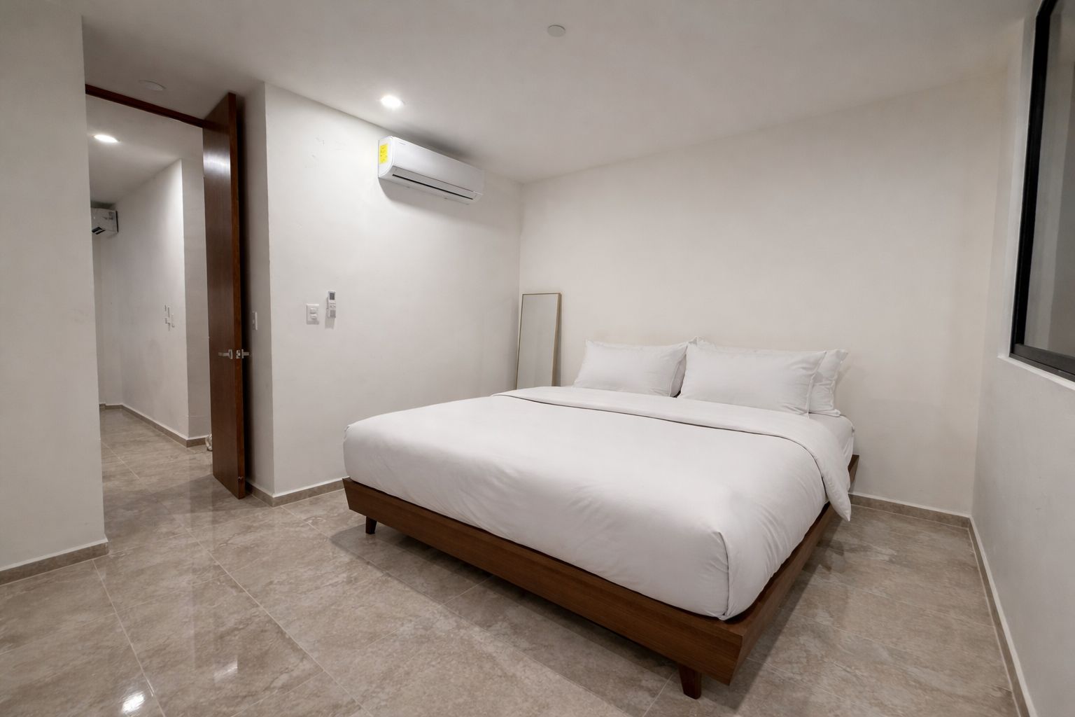 Un dormitorio con cama, una puerta, unidad de aire acondicionado y ventana.