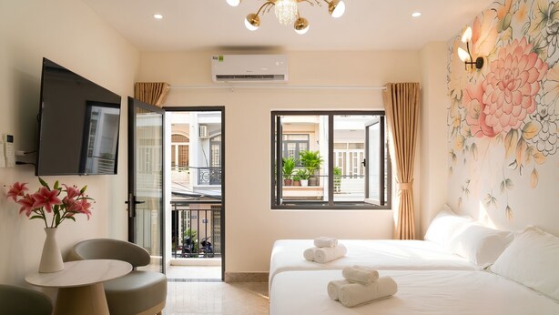 A hotel room with a bed, a TV, a small table with chairs, a vase of flowers, and a window with curtains. - The Pivot Suite Ben Thanh - District 1 (Ho Chi Minh City)