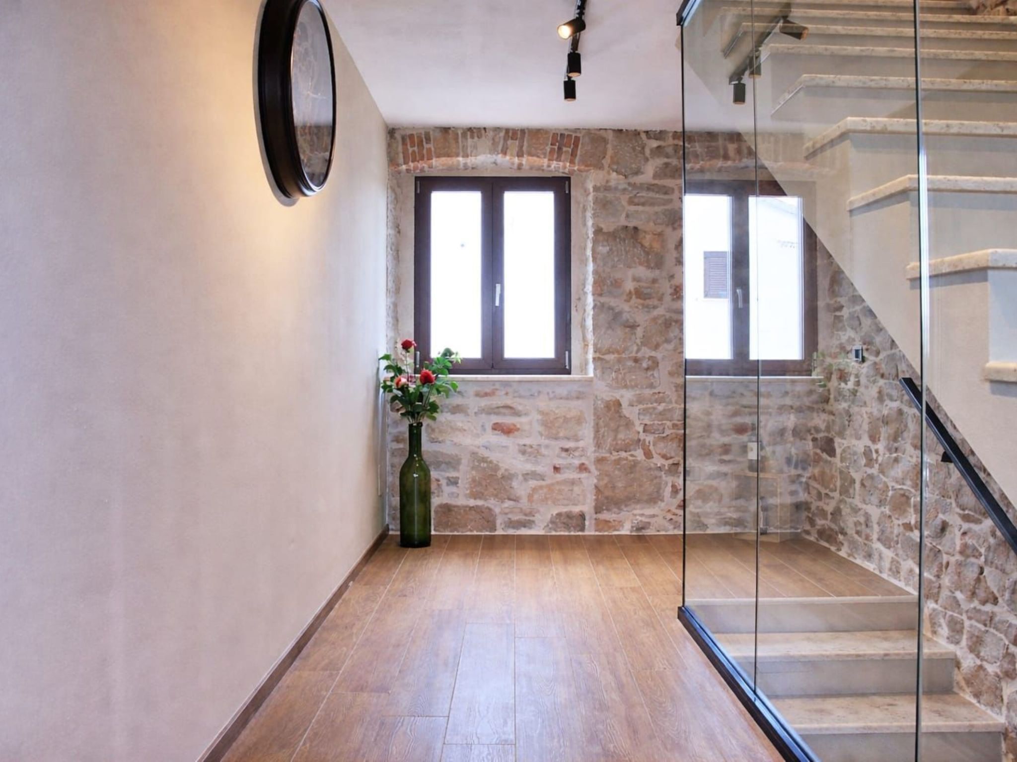 A hallway with a stone wall, a wooden floor, a glass door, and a staircase with a stone wall.