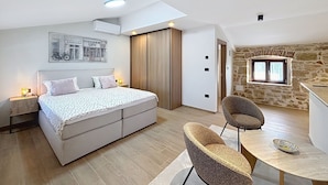 A bedroom with a bed, bedside tables, a chair, a small table, and a stone wall with a window. - Dariocchi by Interhome (Poreč/Kaštelir)