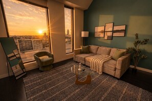 A living room with a sofa, armchair, and coffee table, large windows with a city view, and wall art.