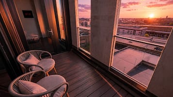 Un balcón con sillones de mimbre y vistas a la ciudad al atardecer.