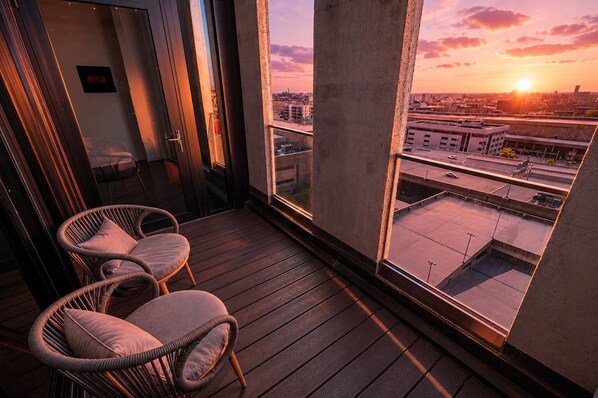 A balcony with wicker chairs and a view of the cityscape at sunset.