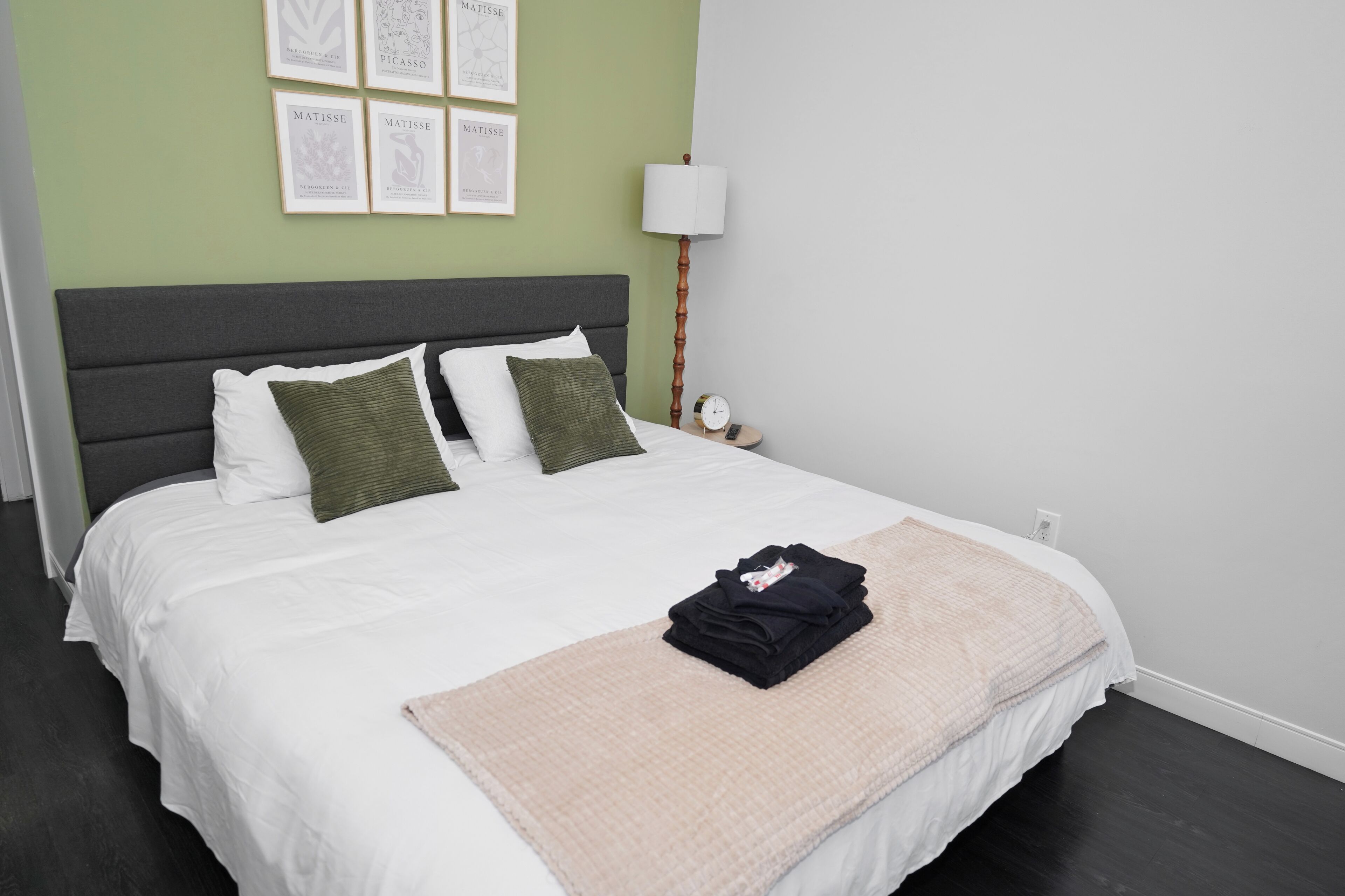 A neatly made bed with a white comforter, two pillows, a folded blanket, and a bedside lamp.