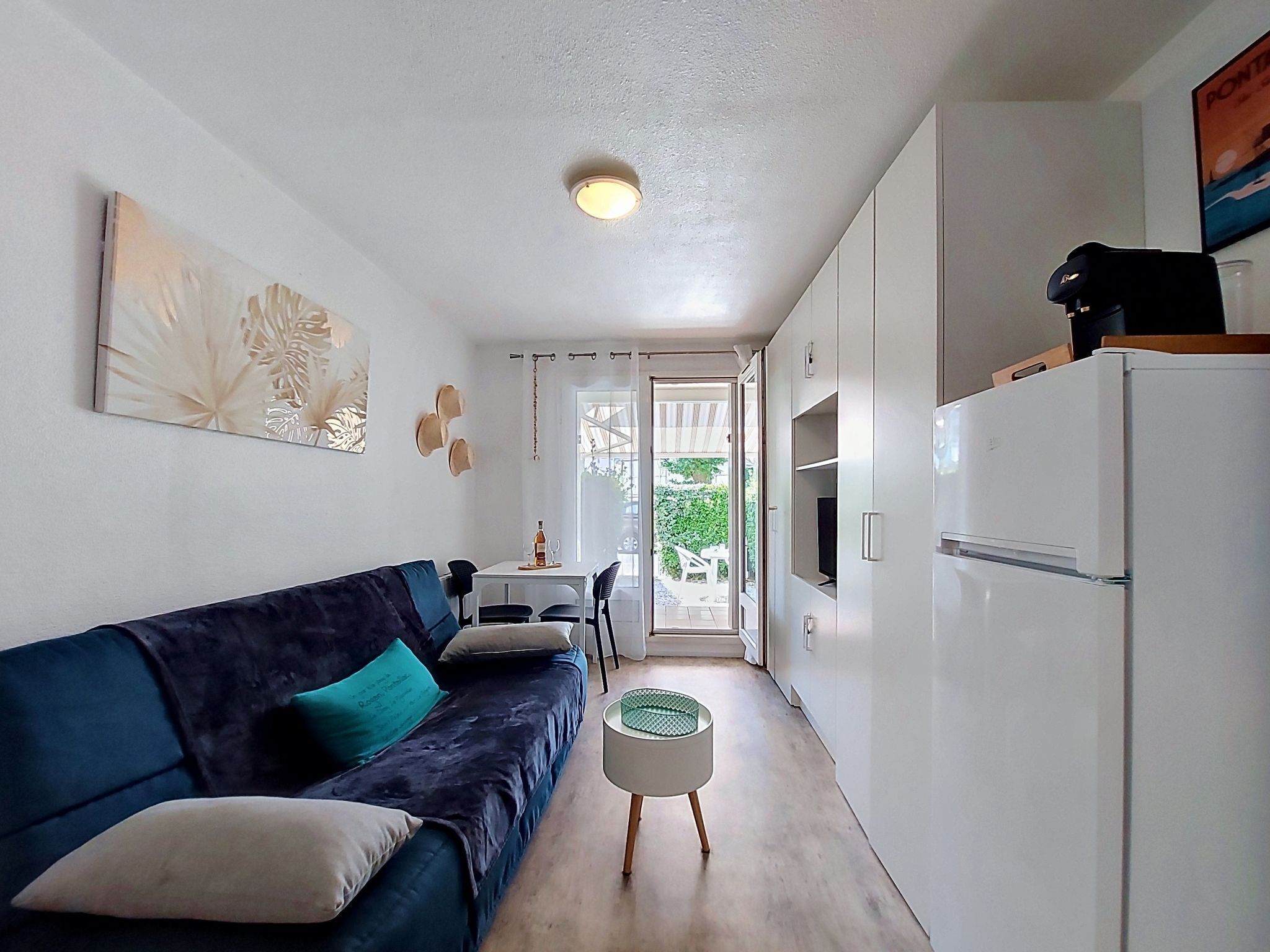 A compact living space with a sofa, a small round table, a refrigerator, and a dining area.