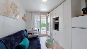 A compact living space with a sofa, a small table, a television, and a kitchenette. - Les Jardins de l'Océan by Interhome (Vaux Sur Mer)