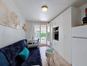 A compact living space with a sofa, a small table, a television, and a kitchenette. - Les Jardins de l'Océan by Interhome (Vaux Sur Mer)