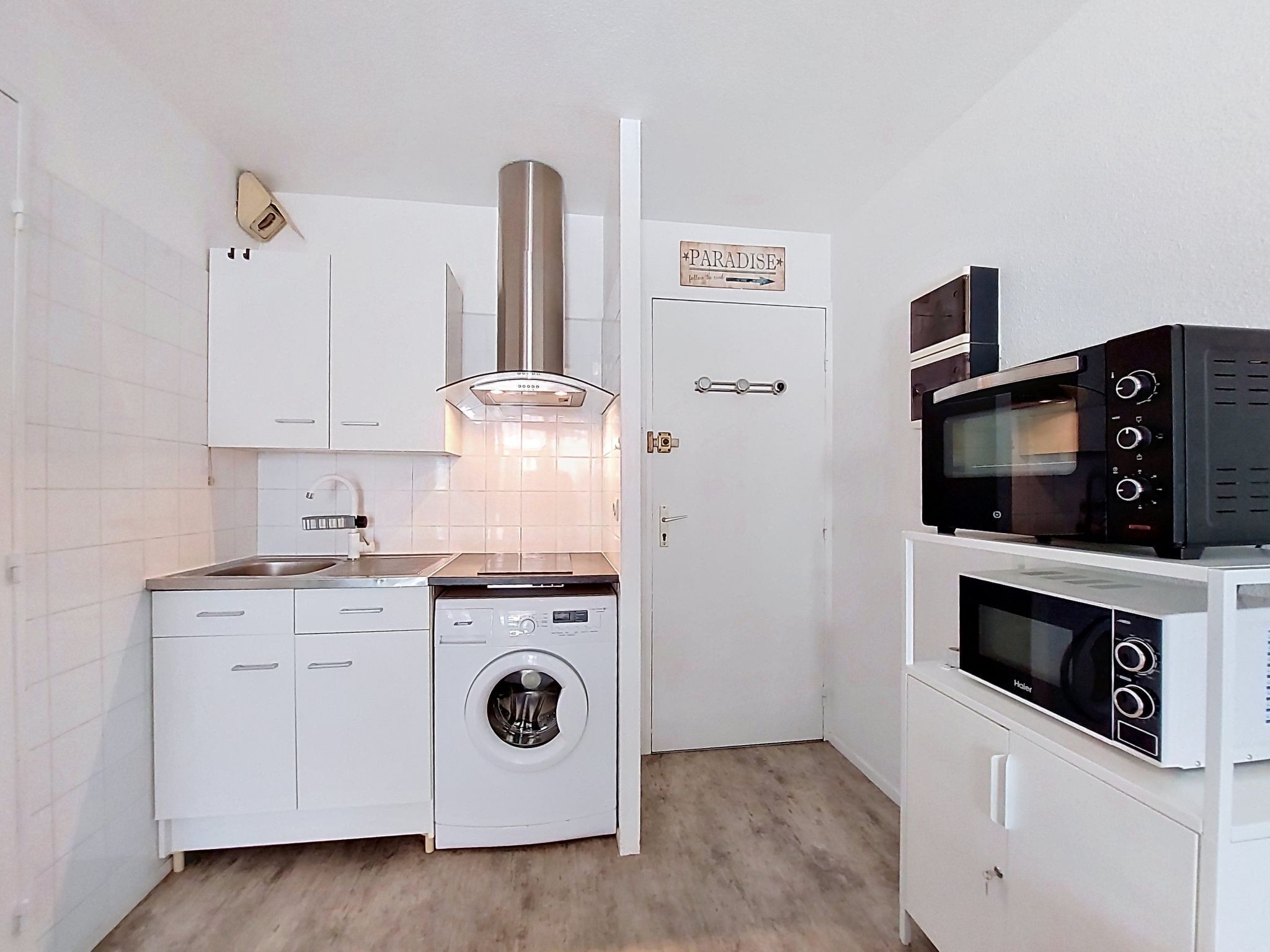 Une cuisine compacte avec des meubles blancs, un four encastré, un four à micro-ondes et un lave-linge.