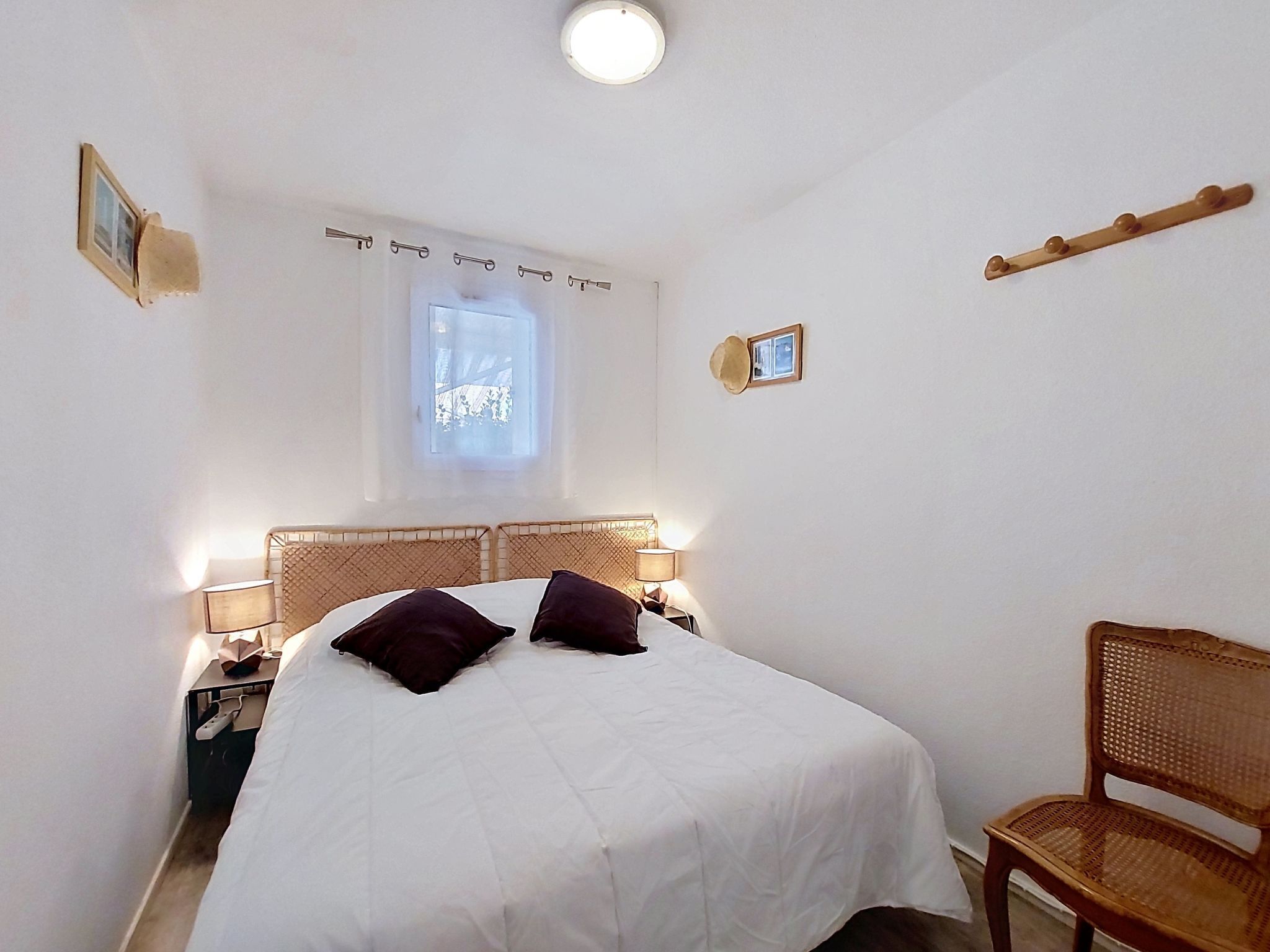 A bedroom with a bed, bedside lamps, a window, a chair, and a small picture on the wall.