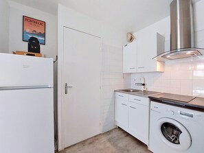 A compact kitchen with a built-in washing machine, a stainless steel range hood, and white cabinetry. - Les Jardins de l'Océan by Interhome (Vaux Sur Mer)