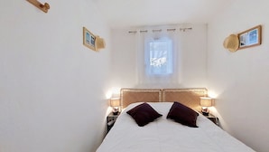 A bedroom with a bed, two bedside lamps, a window with a view, and a wooden headboard. - Les Jardins de l'Océan by Interhome (Vaux Sur Mer)